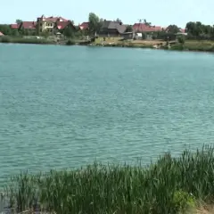 Spalona jezioro z domkami na brzegu. Woda jest turkusowa, a na pierwszym planie rośnie trzcina.