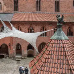 Zwiedzanie zamku w Malborku. Wewnętrzny dziedziniec z ceglanymi murami, dachówkami i nowoczesną instalacją z białej siatki.