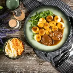 Pyszne niemieckie potrawy: pieczeń w sosie z kluskami ziemniaczanymi i surówką z kapusty i marchewki.
