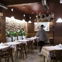 Wnętrze trattorii Mamma Mia, stoły nakryte obrusami w kratę, półki z winami, obraz z rowerem i skuterem.