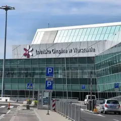 Nowoczesny budynek Lotniska Chopina w Warszawie z charakterystycznym logo. Samochody podjeżdżają do terminalu.