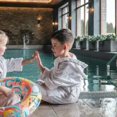 Dzieci w szlafrokach przy basenie, gotowe na wakacje w górach z dziećmi. Zabawa i relaks w górskim spa.