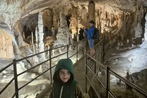 Dziecko w kapturze na ścieżce w jaskini Postojna, gdzie można kupić bilety. Widok na stalaktyty i stalagmity.