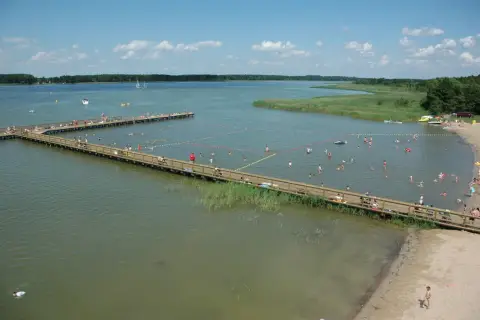 Letnie popołudnie w mieście nad jeziorem. Ludzie kąpią się i odpoczywają na drewnianych pomostach.
