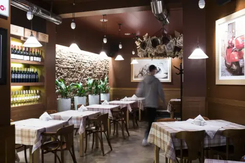 Wnętrze trattorii Mamma Mia, stoły nakryte obrusami w kratę, półki z winami, obraz z rowerem i skuterem.