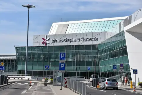 Nowoczesny budynek Lotniska Chopina w Warszawie z charakterystycznym logo. Samochody podjeżdżają do terminalu.