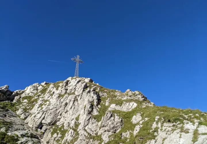 Kamienna ścieżka prowadzi pod górę, gdzie widać krzyż na szczycie. W oddali widać samolot. Kolejka na Giewont to wyzwanie dla każdego turysty.