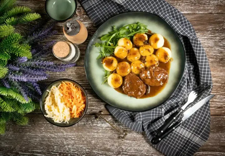 Pyszne niemieckie potrawy: pieczeń w sosie z kluskami ziemniaczanymi i surówką z kapusty i marchewki.