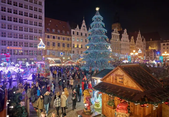 Tłoczny jarmark we Wrocławiu nocą. Rozświetlona choinka, kramy i tłumy ludzi tworzą magiczną atmosferę.