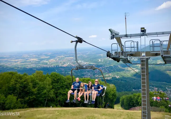 Rodzina na wyciągu krzesełkowym podziwia panoramę Wisły i okolicznych gór.