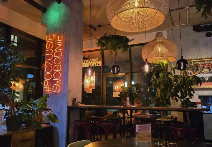 Wnętrze restauracji "Garnizon" z neonem "#POCZUJSIĘ SWOBODNIE", plecionymi lampami i roślinnością.