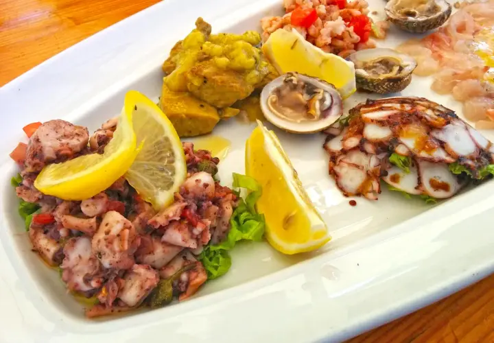 Pyszne dania chorwackie: sałatka z ośmiornicy, krewetki, małże i carpaccio z ryby, ozdobione cytryną.