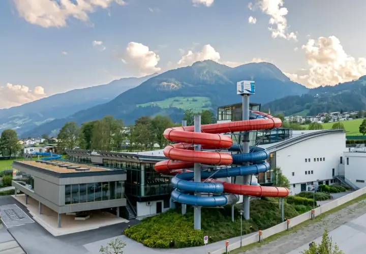 Wodne szaleństwo w Zillertal: kolorowe zjeżdżalnie wodne przyciągają do nowoczesnego aquaparku, w tle majestatyczne góry.