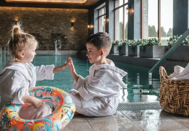 Dzieci w szlafrokach przy basenie, gotowe na wakacje w górach z dziećmi. Zabawa i relaks w górskim spa.