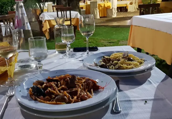 Dwa talerze z makaronem i owocami morza, kieliszki z winem i woda na stole w restauracji pod gołym niebem.