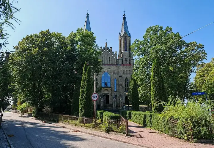 Neogotycki kościół w Krynkach, otoczony zielenią, z wieżami i charakterystycznym oknem.