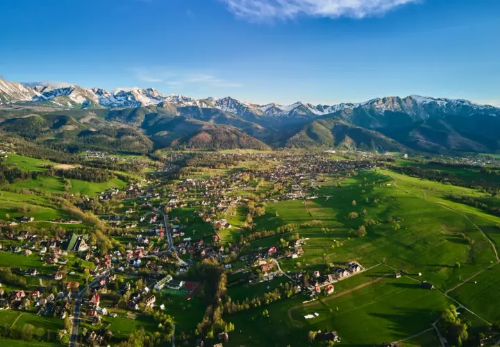 Widok na Zakopane i Tatry. Zielone łąki, zabudowania i ośnieżone szczyty tworzą malownicze okolice Zakopanego atrakcje.