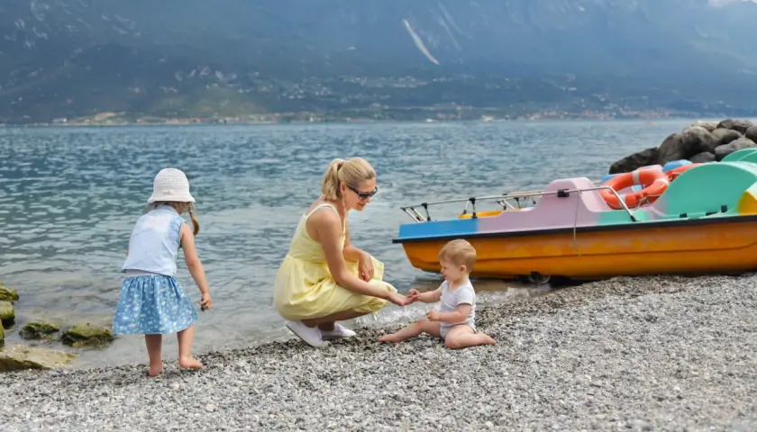 Mama z dziećmi na kamienistej plaży nad jeziorem. W tle góry i kolorowe łódki. Wspaniały dzień nad Gardno.