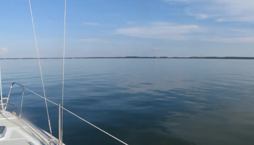 Żegluga po spokojnym mazurskim jeziorze Krzyżówka. Błękitne niebo z chmurkami, linia brzegowa w oddali.
