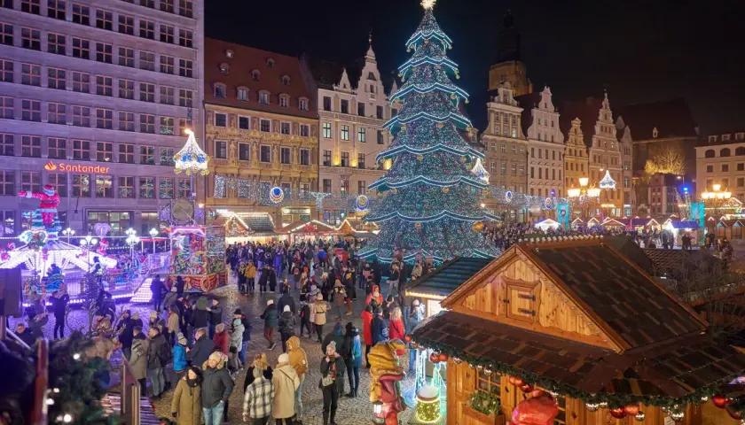 Tłoczny jarmark we Wrocławiu nocą. Rozświetlona choinka, kramy i tłumy ludzi tworzą magiczną atmosferę.