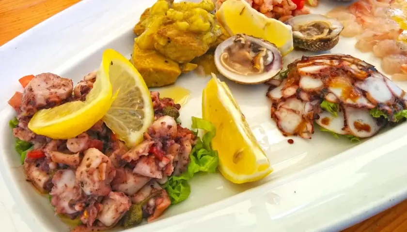 Pyszne dania chorwackie: sałatka z ośmiornicy, krewetki, małże i carpaccio z ryby, ozdobione cytryną.