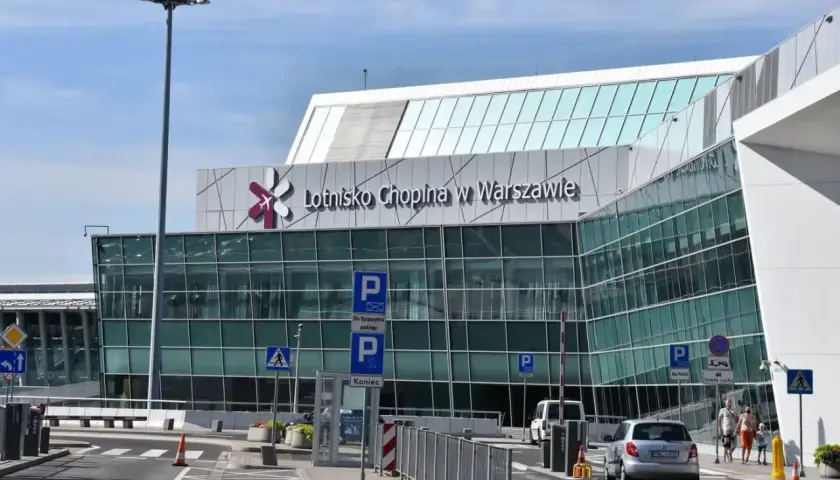 Nowoczesny budynek Lotniska Chopina w Warszawie z charakterystycznym logo. Samochody podjeżdżają do terminalu.