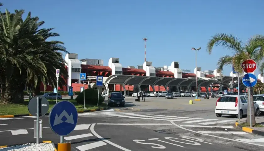 Słoneczny dzień na lotnisku Tropea. Samochody czekają przed terminalem, a palmy szumią na wietrze.