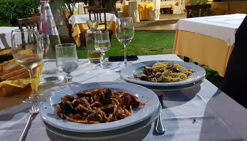 Dwa talerze z makaronem i owocami morza, kieliszki z winem i woda na stole w restauracji pod gołym niebem.