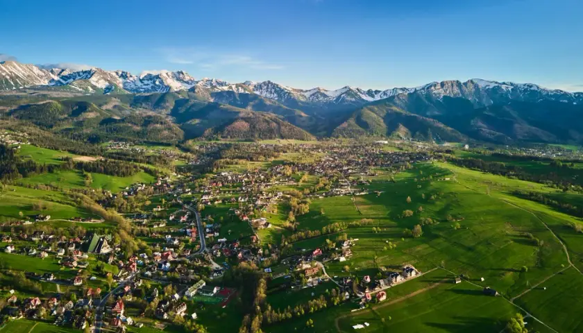 Widok na Zakopane i Tatry. Zielone łąki, zabudowania i ośnieżone szczyty tworzą malownicze okolice Zakopanego atrakcje.