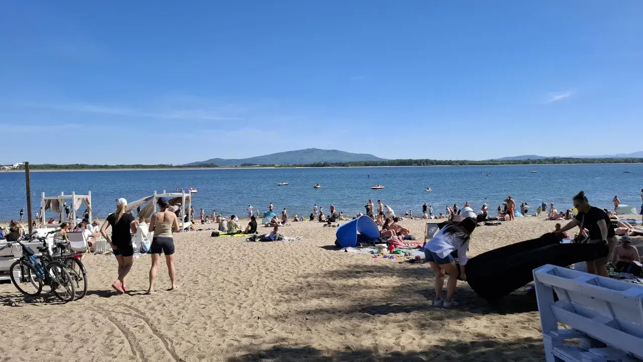Słoneczny dzień nad jeziorem Mietkowskim. Ludzie odpoczywają na plaży, niektórzy kąpią się w wodzie.
