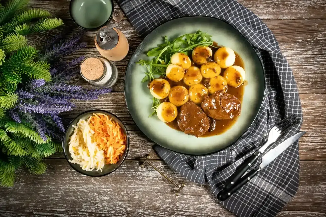 Pyszne niemieckie potrawy: pieczeń w sosie z kluskami ziemniaczanymi i surówką z kapusty i marchewki.