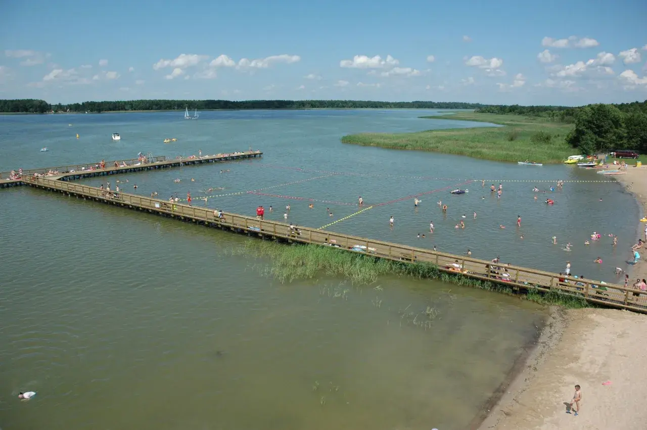 Letnie popołudnie w mieście nad jeziorem. Ludzie kąpią się i odpoczywają na drewnianych pomostach.
