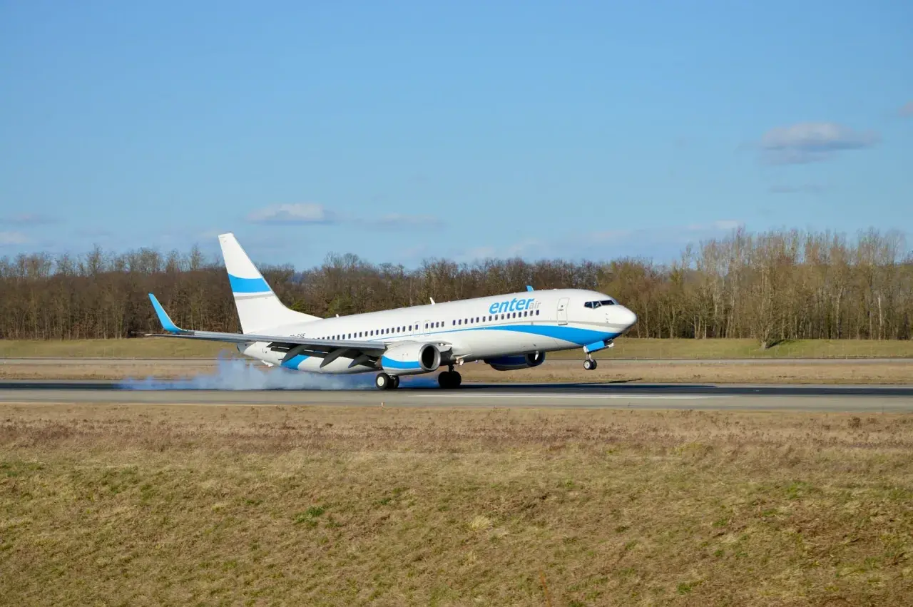 Samolot Enter Air ląduje na pasie startowym, wzbijając tumany kurzu.