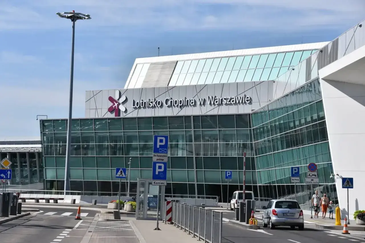Nowoczesny budynek Lotniska Chopina w Warszawie z charakterystycznym logo. Samochody podjeżdżają do terminalu.