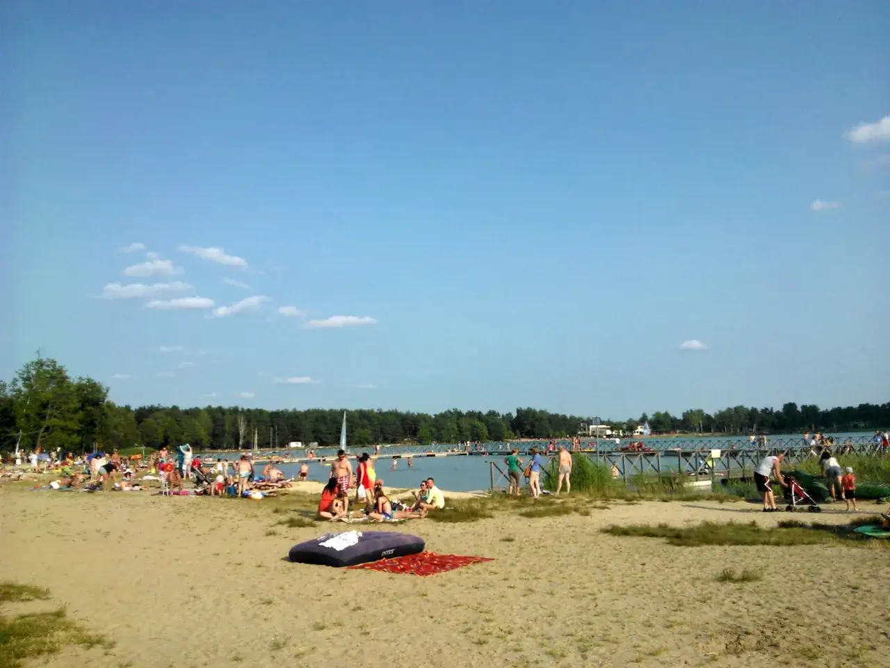 Plaża nad jeziorem, ludzie odpoczywają i kąpią się. Jezioro Białe atrakcje to słońce, woda i relaks.