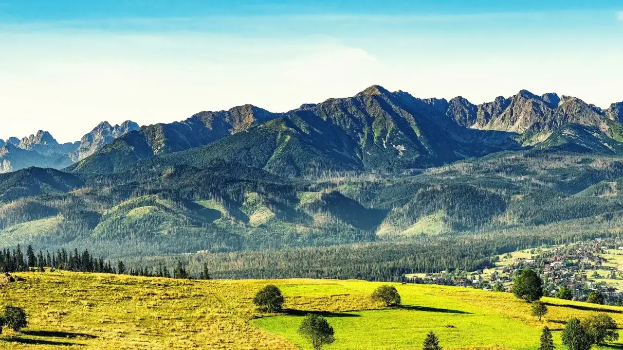 Widok na Tatry z zielonymi łąkami i lasami. W oddali majaczy Bachledzki Wierch, a u podnóża gór rozciąga się malownicza wieś.