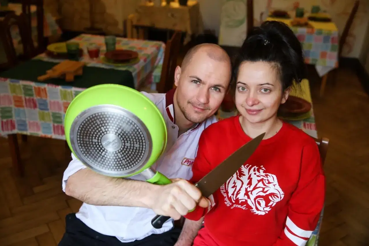 Para w restauracji, on trzyma zieloną patelnię, ona nóż. Kolorowe patelnie restauracja.